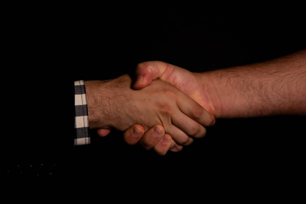 two man shaking hand in a black background one have coat suit