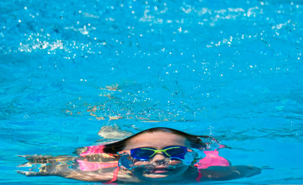 Young girl is holding her breath and swimming underwater in a bright blue pool