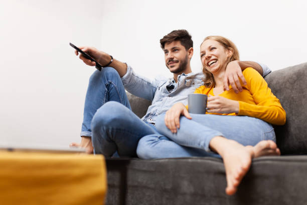 istock couple in love sitting on a sofa watching tv. holding coffee and remote control 2153245899