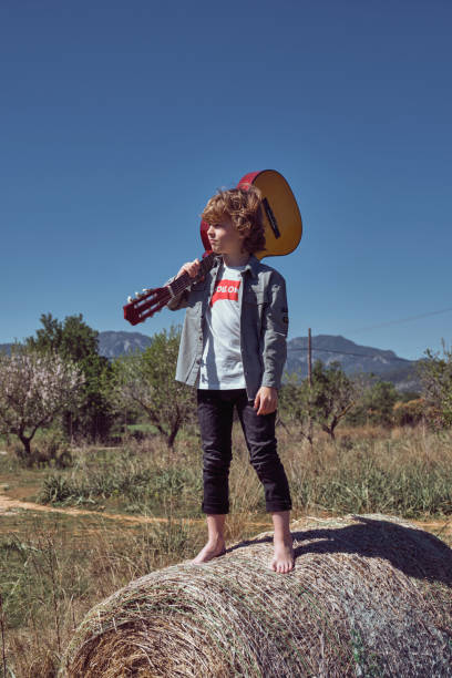 istock Calm little boy standing on haystack with guitar in hand and loo 2153249073