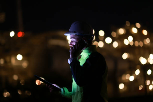 istock Smart  engineer with green safety jacket works on a digital tablet and using a mobile phone at the refinery plant during night shift 2153256922