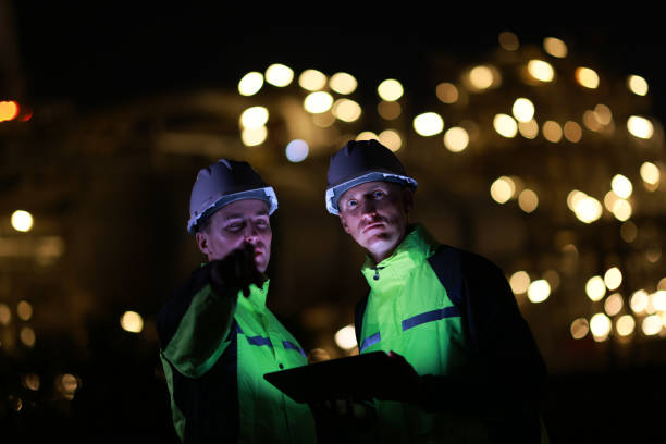 istock Two energy engineers using digital tablets for work and discussing the background of oil refinery distillation plants and bokeh light at night time. 2153256963