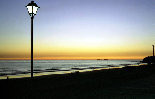 street lamp lit on a beach against the sunset sky