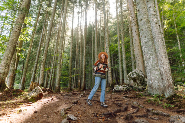 istock Young female traveler with backpack standing in forest with tall coniferous trees. 2153276494