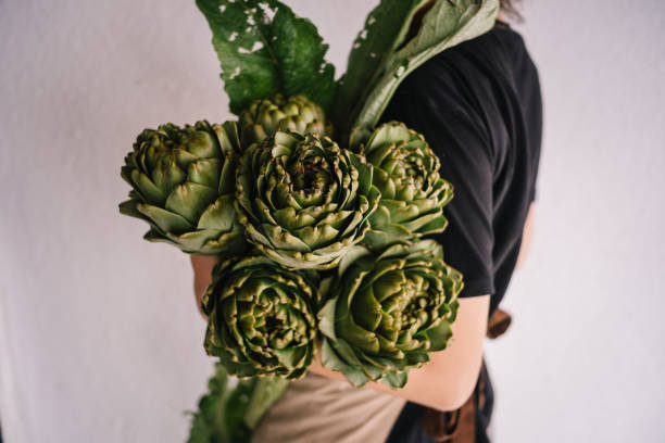 Young woman is holding a bunch of artichokes in front of a white wall.