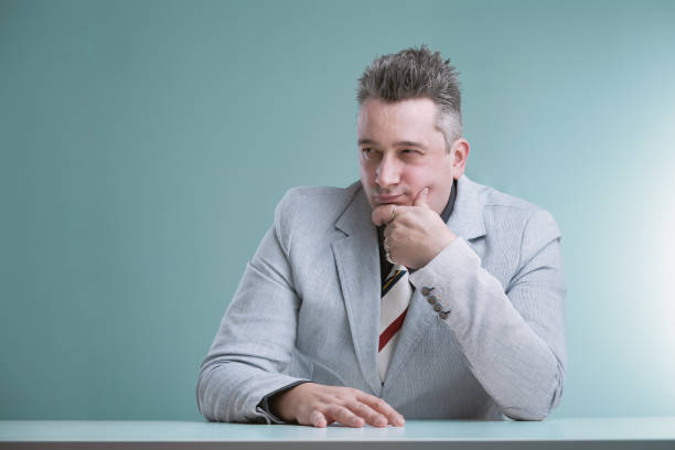 Pensive professional in grey suit with spiked hair appears contemplative, hand on chin, reflecting quietly