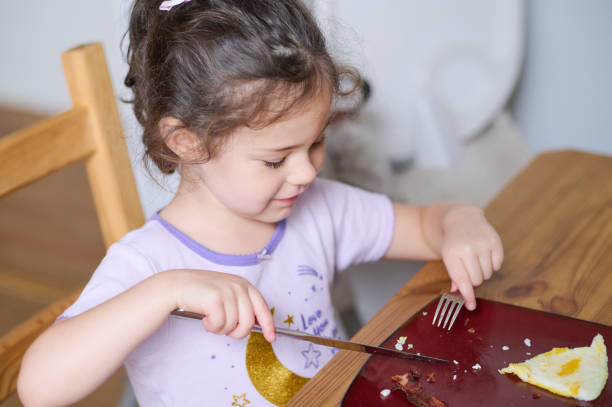 istock Young pretty girl eating eggs and bacon with knife and fork for the first time 2153302546