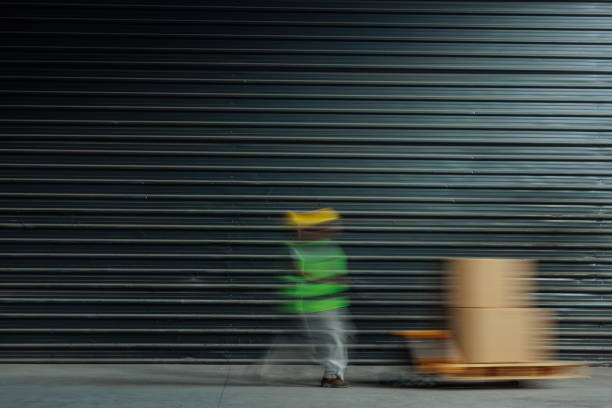 Motion blur of an African-American worker pushing a pallet jack along a concrete floor in a factory setting.