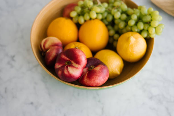Fresh fruit, peaches, grapes and oranges in a plate on the marble table in the kitchen. Healthy and wholesome food