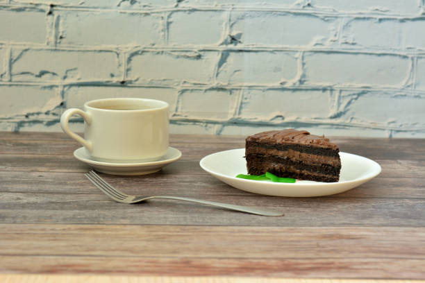 istock A piece of fresh chocolate biscuit cake on a plate decorated with mint leaves, a fork and a cup of hot black coffee on a light wooden table. 2153318727