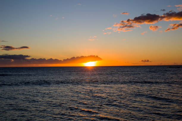 Vast shot of hanalei bay's view of a sunset falling on mountain and sea, cloudy sky above. Taken in Kauai, Hawaii, during the day.