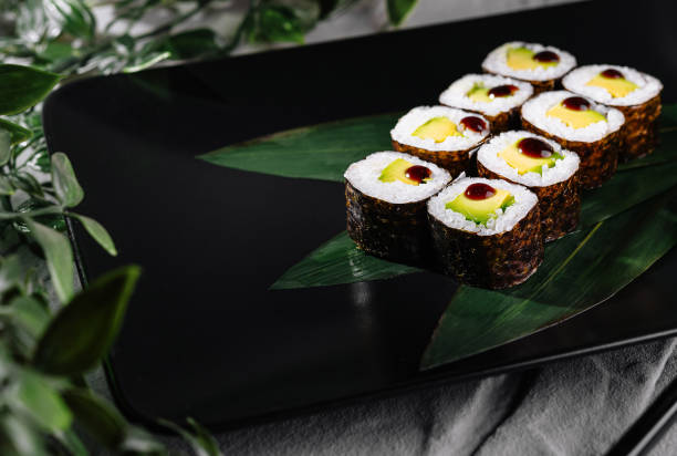 istock Sushi rolls garnished with wasabi and ginger on a modern black plate, botanical backdrop 2153335190