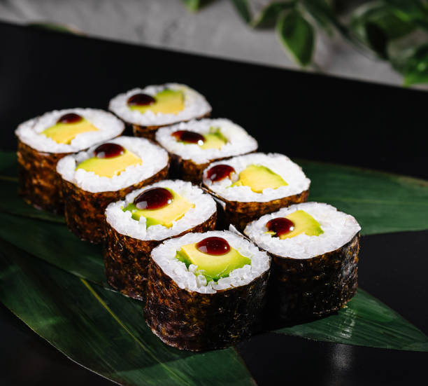 istock Sushi rolls garnished with wasabi and ginger on a modern black plate, botanical backdrop 2153335551