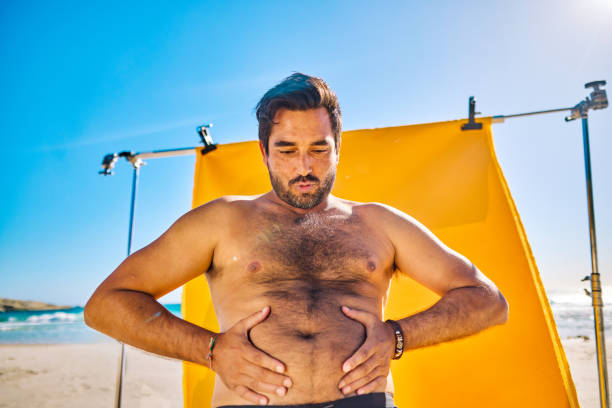 istock New Masculinity: Shirtless man posing on the beach with yellow backdrop. Bright sunny day with blue sky. Masculinity and body positivity concepts. 2153338232
