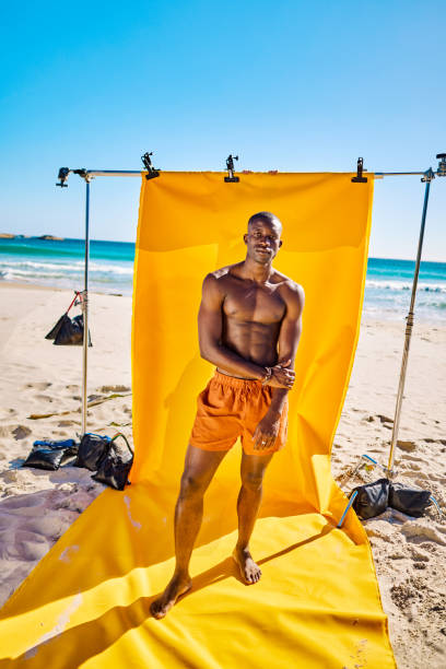 istock New Masculinity: Shirtless man posing on the beach with yellow backdrop. Bright sunny day with blue sky. Masculinity and body positivity concepts. 2153338242