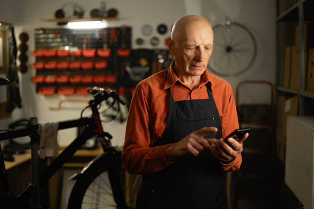 istock Old mechanic working in garage using smartphone to browse social media 2153338376