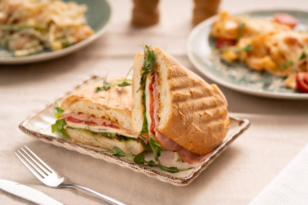 Toasted panini with ham, cheese and lettuce sandwich on plate serving on table with another dishes for breakfast