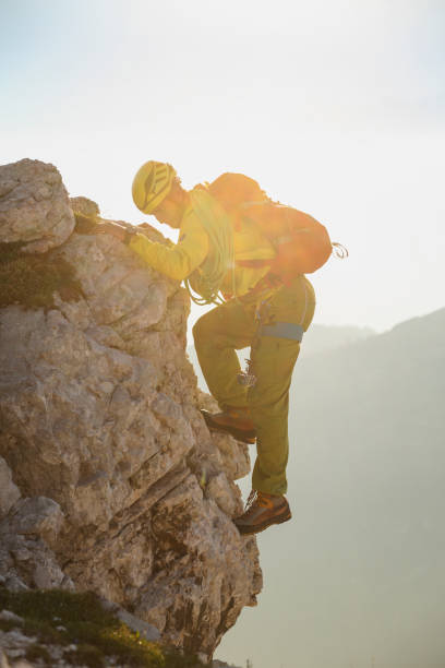 Mountain climber with climbing equipment (rope, backpack, helmet, hood,...) against the sun and blue sky. Climbing up the mountain.