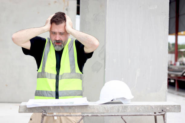 istock Panic attacks senior worker engineer foreman with safety vest and helmet put hands on head while staring at blueprint at construction site. Stressed elderly architect works at building site workplace. 2153350157
