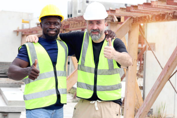 istock Happy harmony worker at workplace, smiling white foreman and African engineer cuddle around necks and give thumbs up at construction building site. Love and respect in differences of race, diversity 2153350376