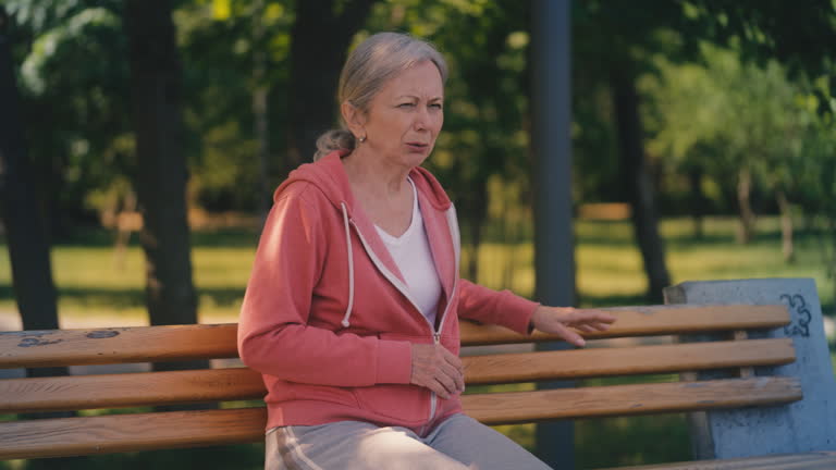 Tired senior woman sits on bench after jogging in park, resting post-sport