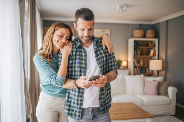 istock Cheerful couple looking together at mobile phone at home 2153356511