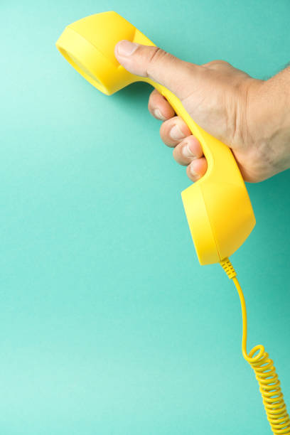 istock Retro yellow telephone receiver held by a hand on a striking turquoise background: nostalgic communication. 2153361228