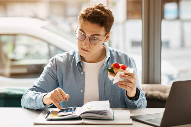 Curly-haired young man with glasses multitasking by eating a healthy wrap