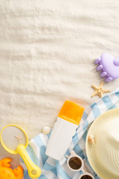 istock Top vertical view of a sandy beach setup featuring children's toys, sunscreen, a straw hat, and sunglasses for a family vacation 2153365312