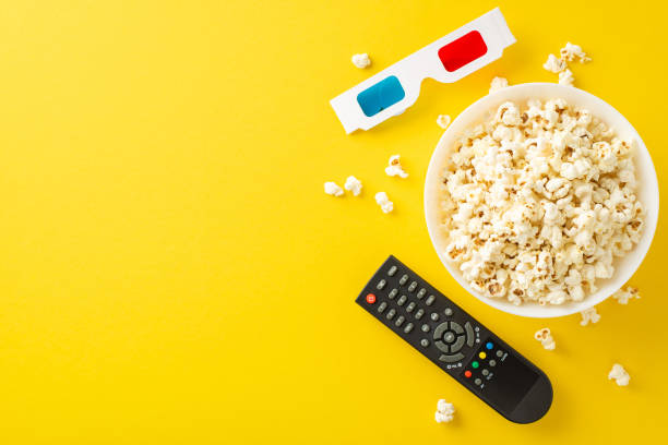 istock Cozy home cinema top view scene: pop corn snack, 3D glasses, and remote control on a yellow surface 2153365351