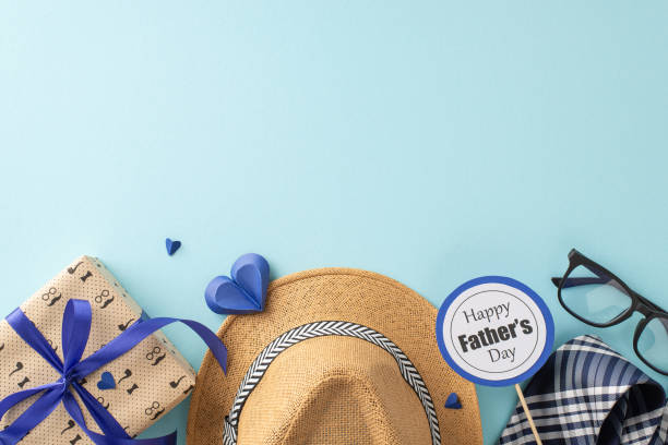 istock Personalize your Father's Day message with a top-view arrangement highlighting a straw hat, elegant necktie, gift box, glasses, postcard, and paper hearts on a soothing pastel blue scene 2153365354
