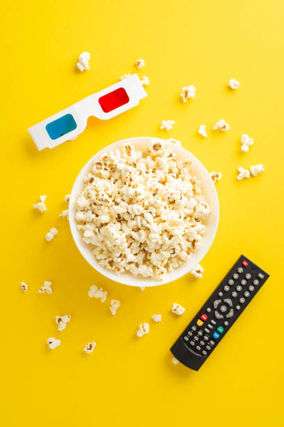 istock Casual home theater experience awaits with popcorn. Equipped for online streaming, complete with 3D specs and remote. Vertical top view of movie-themed items add festive touch on yellow background 2153365367