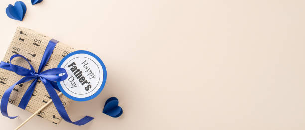 istock A thoughtful Father's Day gift box wrapped in paper and a blue ribbon, adorned with decorative blue hearts and a labeled stick on a soft light beige backdrop 2153365405