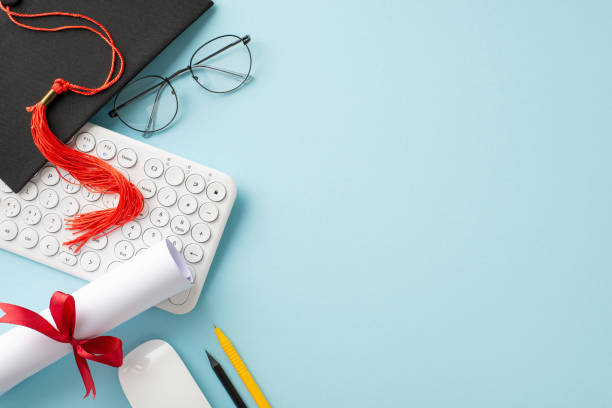 istock Online education completion theme. Overhead shot of keyboard, mouse, mortarboard, diploma, study materials, spectacles on soft blue backdrop with space for text or promotion 2153365467