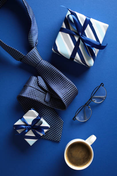 istock Flat lay composition featuring a cup of coffee, two gift boxes, glasses, and a neatly folded blue tie on a vibrant blue background. Ideal for topics related to gift-giving, men’s fashion, Fathers Day 2153367172
