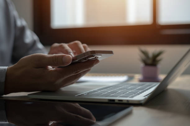 istock A person is using a cell phone while sitting at a desk with a laptop and a potted plant. Concept of productivity and focus, as the person is engaged in work or communication on their devices 2153367220