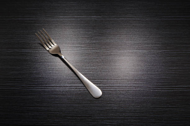 A single fork isolated on top of black wooden background copy space