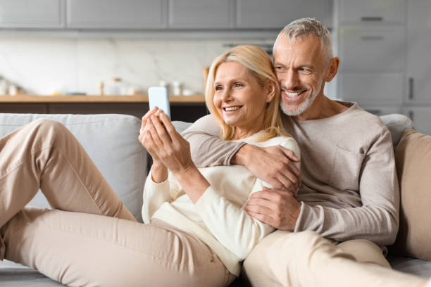 istock Happy senior couple sitting on sofa at home, using smartphone 2153370951