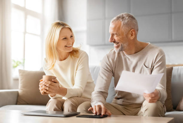 istock Senior spouses paying bills online from home, sitting on couch 2153371097