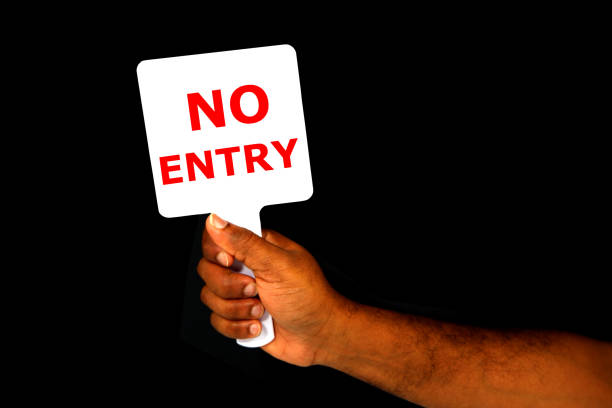 NO ENTRY Sign board holding hand on black background close-up view