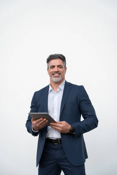 istock Middle age mature businessman using pc tablet for business work application. Smiling handsome older man in formal suit holding touchscreen device looking aside. Isolated white background, Vertical 2153377116