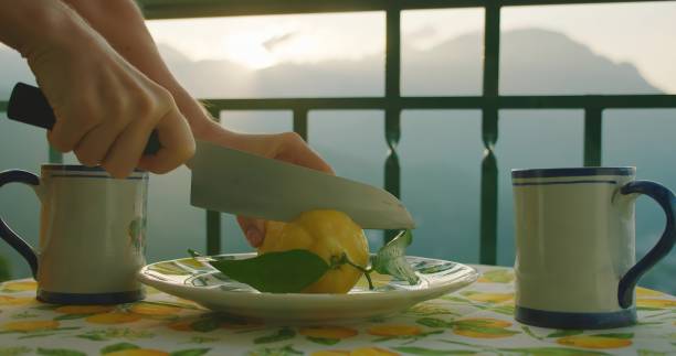 istock Hands slice a lemon at a balcony table during sunrise. Precise cuts release the zest's aroma, serene morning landscape of mountains. 2153377487