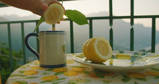 istock A hand squeezes lemon juice into a cup on a table with a citrus-themed cloth. The table setting reflects a simple, refreshing morning ritual. 2153378040