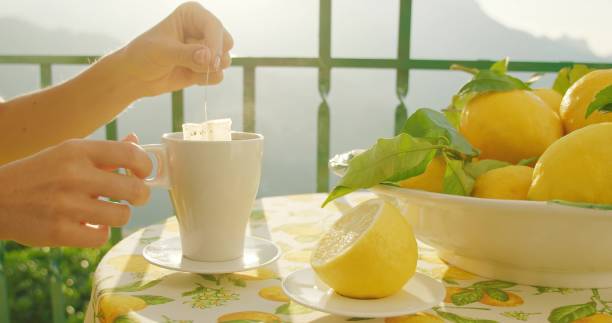 istock Hands steep a tea bag into a mug beside a lemon bowl. Morning ritual captures steeping tea with fresh lemons in soft focus. 2153378378