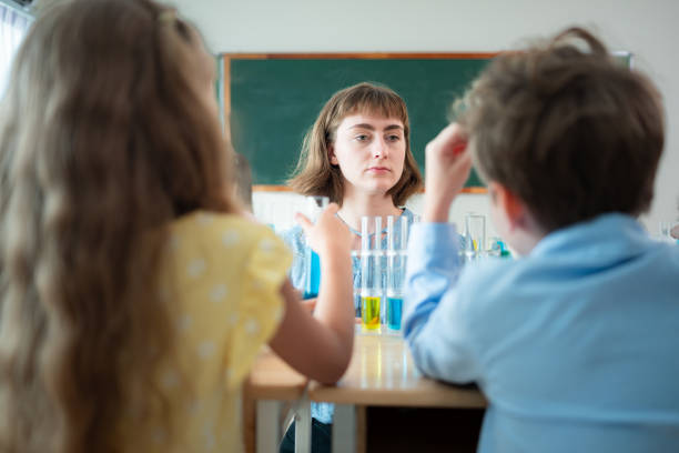 Teacher interacting with young students in a science lab. They are wearing lab coats and engaging in experiments.