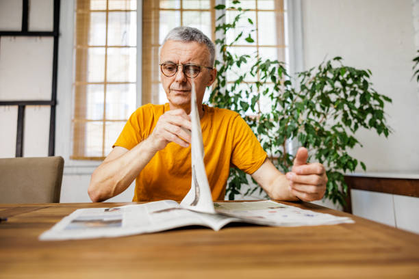 Slim mature man reading newspapers at home