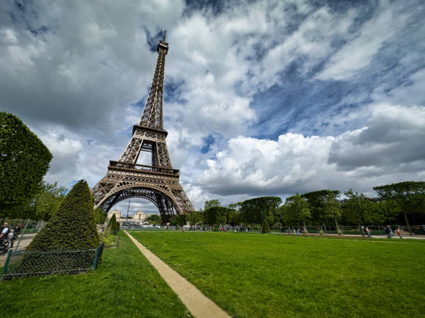 A beautiful view of the Eiffel Tower in Paris, surrounded by lush greenery under a moody overcast sky. The composition highlights the area’s charm, adorning Paris's scenic beauty.