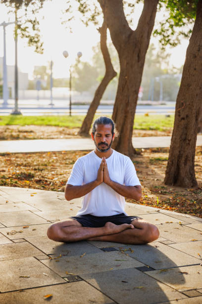 istock Indian man sitting on ground in public park with hands clasped before yoga practice 2153397521