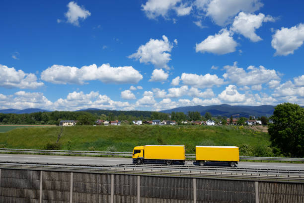 yellow lorry with trailer passes Deggendorf on the A3 motorway, background Bavarian Forest, Lower Bavaria, Germany