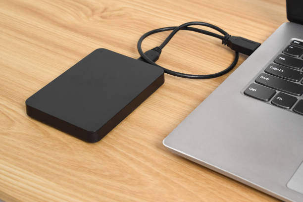 istock External backup hard disk drive connected to laptop on wooden table 2153405102